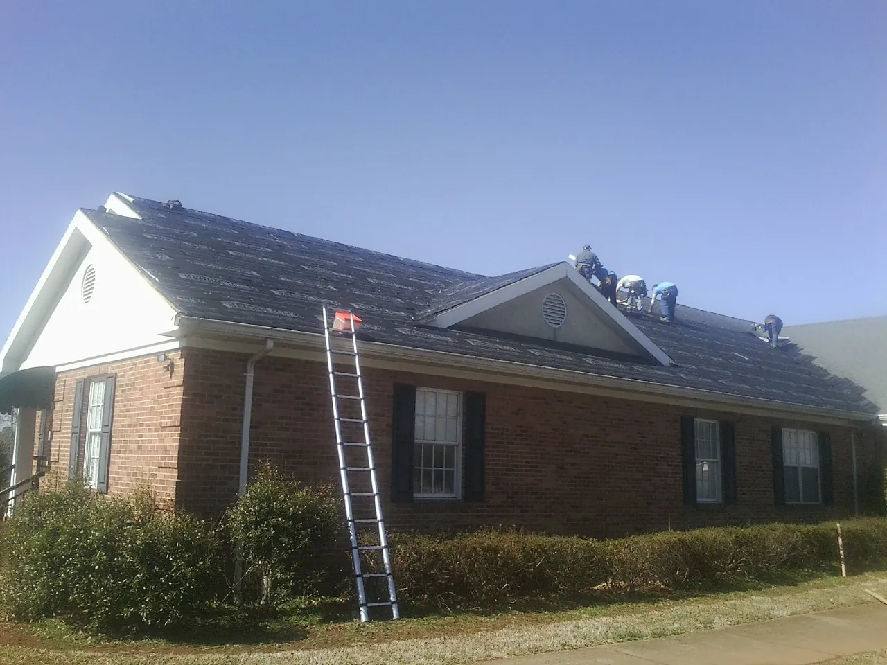 Crew tearing shingles off a brick ranch roof with a ladder set — Metal Roof Repair work by our crew in Hansville