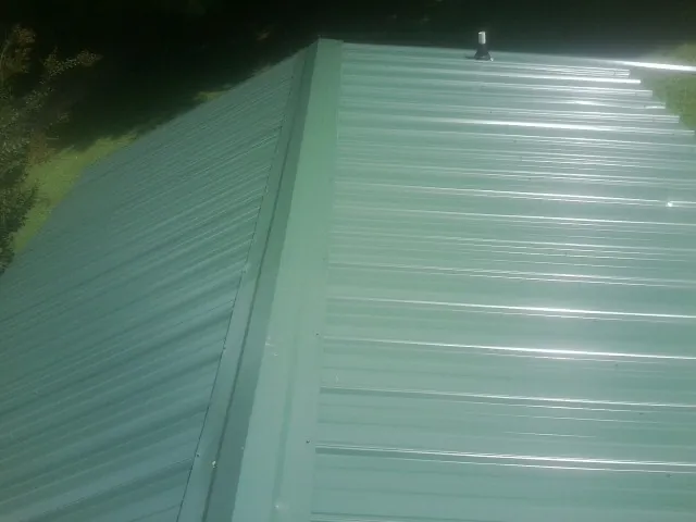 New green metal panels meeting at the ridge of a roof — Flat Roof Repair work by our crew in Hansville