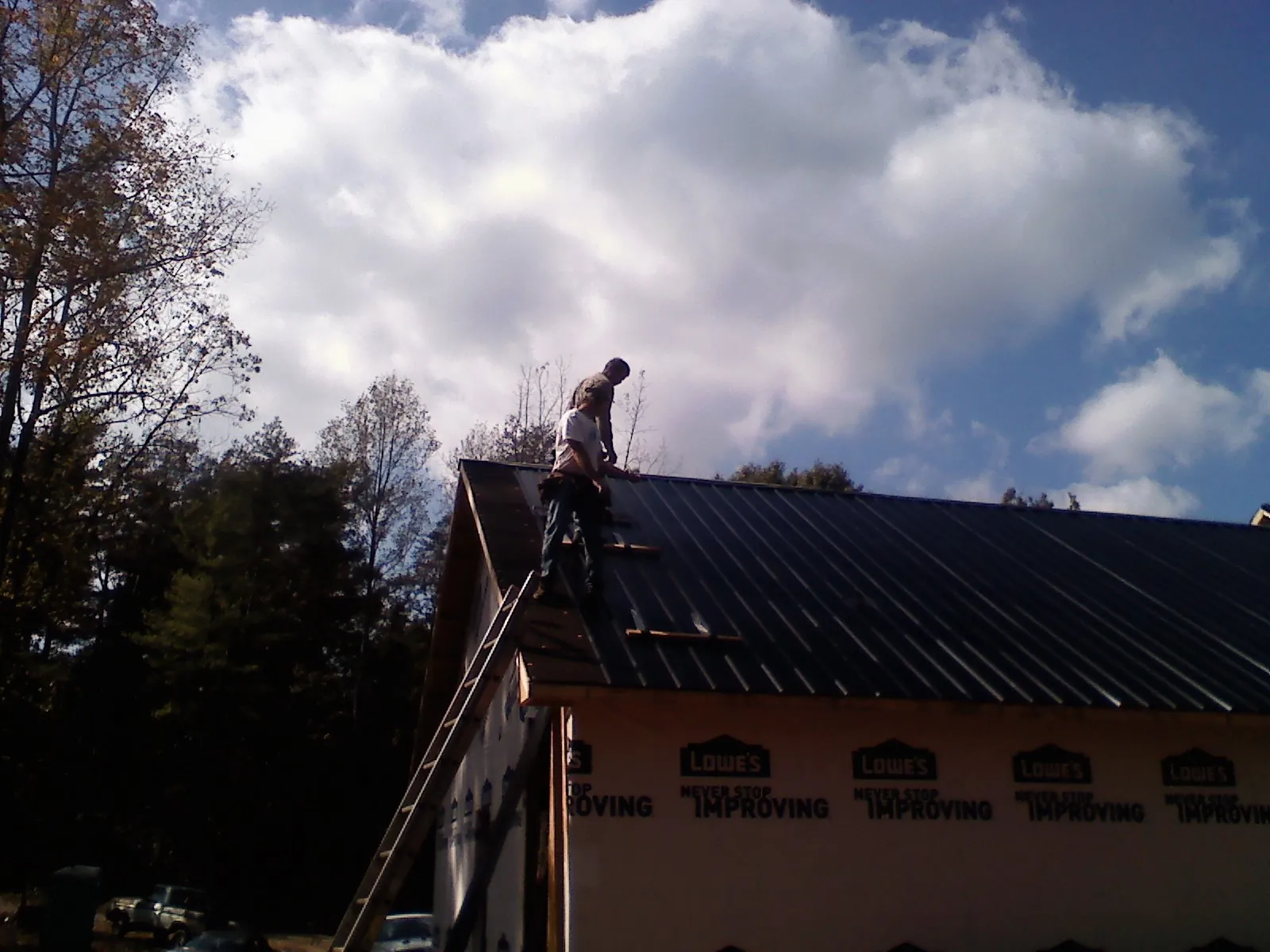 Roofer fastening dark metal panels high against a cloudy sky, from a Roof Inspection job in Hansville