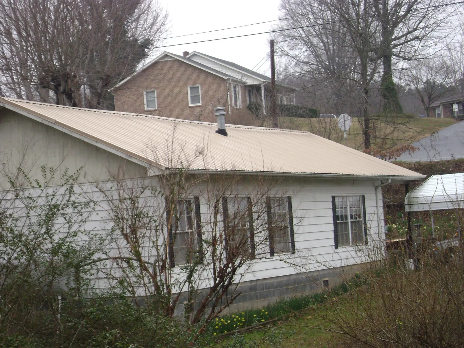 Tan metal roof on a white sided house set into a hillside — Commercial Roofing by Roofing Brothers in Hansville